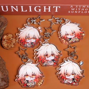 May include: Several clear acrylic keychains featuring a cartoon character with white and red hair, orange eyes, and a red outfit. Each keychain has a silver star-shaped charm and a silver keyring. The background is a warm brown color.