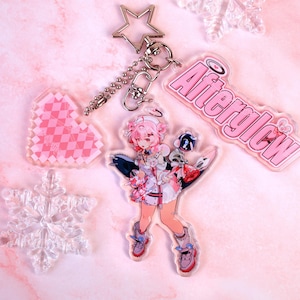 Puede incluir: Un llavero de acrílico con un cierre en forma de estrella, un dije de corazón rosa con patrón de cuadros, un dije de copo de nieve transparente, un personaje de pelo rosa con una bomba y un dije de texto rosa que dice Afterglow.