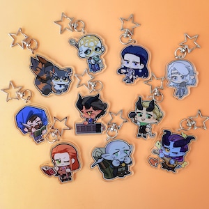 Può includere: Una collezione di portachiavi con personaggi con attacchi a forma di stella. I portachiavi presentano varie figure di cartoni animati in diverse pose e abiti, con una varietà di colori. Lo sfondo è di colore arancione.