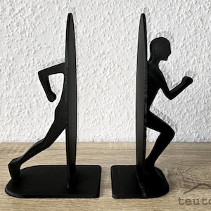 Op de afbeelding: Zwarte metalen boekensteunen met een silhouet van een rennende figuur. De boekensteunen hebben een rechthoekige basis en een verticale steun die het lichaam van de loper vormt. Minimalistisch en modern ontwerp, geschikt voor thuis of op kantoor.
