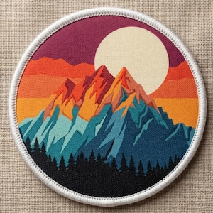 May include: A round embroidered patch featuring a mountain range scene. The design includes a large cream-colored sun, mountains in shades of orange, red, and blue, and a forest at the base. The patch is bordered with white stitching.