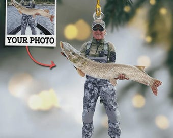 May include: A custom hanging ornament featuring a person wearing a cap, sunglasses, and camouflage fishing gear while holding a large northern pike fish. A small inset square shows the same image with the text YOUR PHOTO below it.