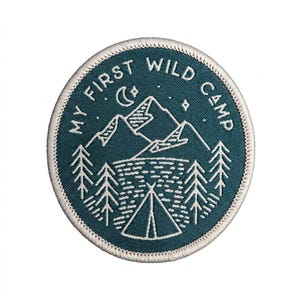 May include: Round teal patch with white embroidered design. The patch features a mountain range, a crescent moon, stars, pine trees, and a tent. The text "MY FIRST WILD CAMP" is embroidered around the edge of the patch.