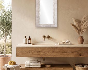 May include: A rectangular wall mirror featuring a textured, off-white woven fabric frame with a decorative border of small, raised white knots surrounding the reflective glass surface. The mirror has a clean, simple design with a neutral colour palette.
