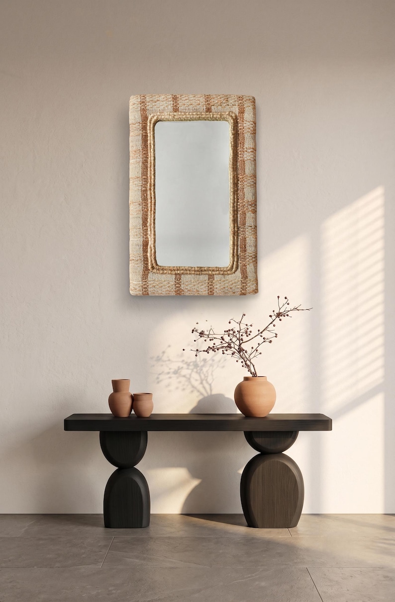 May include: A rectangular wall mirror featuring a thick, textured frame woven from natural fibres in alternating shades of beige and light brown. The mirror has rounded corners and a reflective glass surface centred within the woven border.