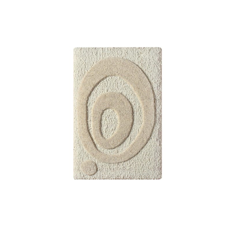 May include: Rectangular beige bath mat with a raised, abstract design of concentric circles in a lighter beige hue. A small, circular accent is positioned below the circles. The mat has a textured surface.