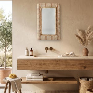 May include: A rectangular wall mirror featuring a woven, textured frame with alternating light beige and brown vertical striped patterns. The mirror has a clean, reflective glass surface and is mounted on a wall above a wooden vanity counter.