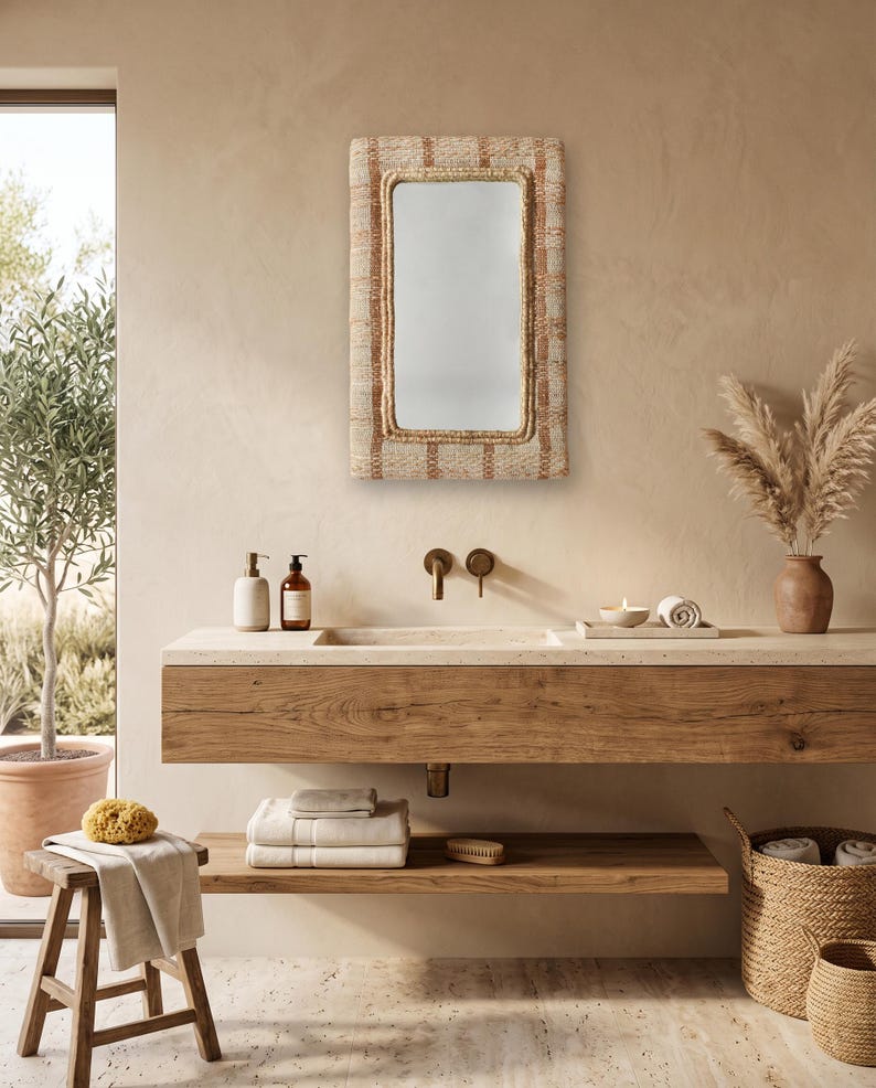 May include: A rectangular wall mirror featuring a woven, textured frame with alternating light beige and brown vertical striped patterns. The mirror has a clean, reflective glass surface and is mounted on a wall above a wooden vanity counter.