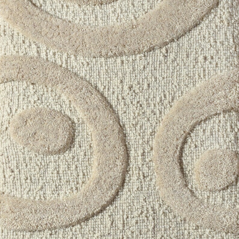 May include: Close-up of a beige bath mat with a textured surface and raised, swirling patterns in a lighter beige color. The design features large, rounded shapes, creating a soft and inviting aesthetic. This bathroom accessory adds a touch of elegance.