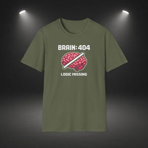 Op de afbeelding: Olijfgroen t-shirt met de tekst "BRAIN:404" boven een gepixelde hersengrafiek die met een witte lijn is doorgestreept. Onder de hersengrafiek staat de tekst "LOGIC MISSING".