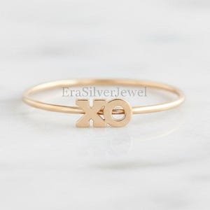 May include: A delicate gold ring featuring the letters "XO" in a minimalist design. The ring is thin and elegant, perfect for everyday wear. The ring is a simple yet stylish accessory.