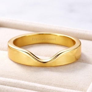Puede incluir: Un anillo dorado con un diseño curvo, presentado en una caja de joyería blanca. El anillo tiene una superficie lisa y pulida y una forma única. El texto "EraSilverJewel" es visible en el anillo.