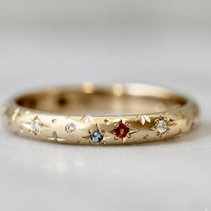 May include: A gold ring with a celestial design. The ring features embedded gemstones in various colors, including clear, blue, and red. The band is adorned with star and leaf patterns, creating a unique and elegant look. The ring is a piece of jewelry.