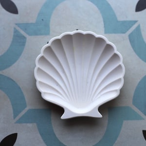 Peut inclure: Un plat en céramique blanche en forme de coquille Saint-Jacques. Le plat est lisse et brillant.