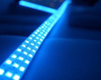 May include: A flexible LED strip emitting bright blue light. The strip is composed of numerous small, square LED lights. The background is a dark blue, with a blurred cityscape visible through a window.
