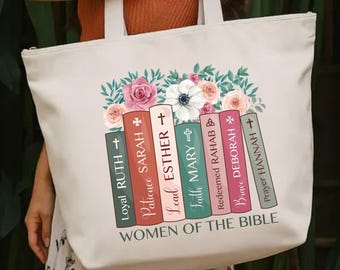 May include: Cream-colored tote bag featuring a floral design above a stack of books. The books are labeled with names like "Ruth" and "Sarah" and the text "Women of the Bible". The bag has white handles and a zipper closure.