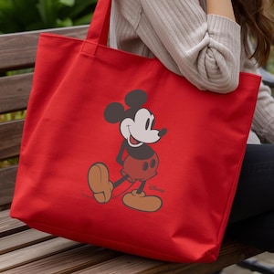 Puede incluir: Un bolso tote rojo brillante con un dise&ntilde;o de Mickey Mouse. El bolso tiene forma rectangular y dos asas. La ilustraci&oacute;n de Mickey Mouse es en negro, blanco y rojo, con el logotipo de Disney en la parte inferior.