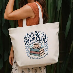 May include: Cream-colored tote bag with the text "Anti Social Book Club" in a circular design. The design includes a stack of books, a coffee cup, and the phrase "Making friends with characters, not people."