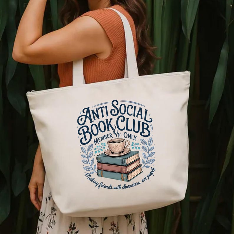 May include: Cream-colored tote bag with the text "Anti Social Book Club" in a circular design. The design includes a stack of books, a coffee cup, and the phrase "Making friends with characters, not people."
