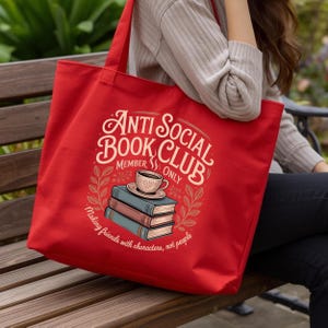 May include: A red tote bag with the text "Anti Social Book Club Member Only" in a vintage style. The design includes a stack of books, a coffee cup, and the phrase "Making friends with characters, not people."