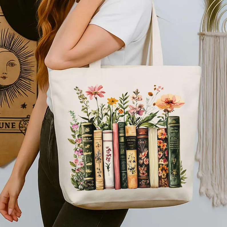 May include: Cream-colored tote bag featuring a watercolor design of colorful flowers and vintage books. The books are in various colors and styles, with floral accents. The bag has sturdy handles for carrying.