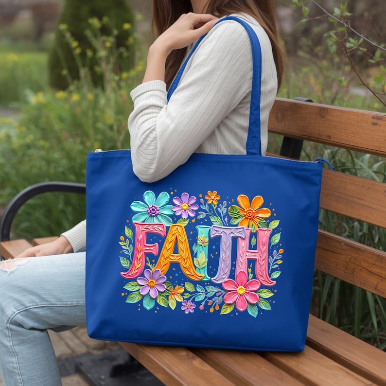 May include: A blue tote bag with the word "FAITH" in colorful, floral-decorated letters. The bag features a zipper closure and handles. The design includes flowers in shades of pink, orange, blue, and purple.