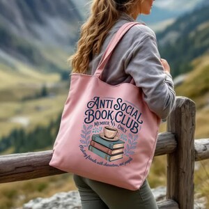 May include: A pink tote bag with the text "Anti Social Book Club Member Only" and a graphic of books and a coffee cup. The bag also has the text "Making friends with characters, not people". The bag is being carried outdoors.