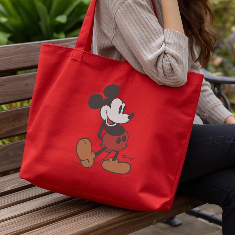 Puede incluir: Un bolso tote rojo brillante con un dise&ntilde;o de Mickey Mouse. El bolso tiene forma rectangular y dos asas. La ilustraci&oacute;n de Mickey Mouse es en negro, blanco y rojo, con el logotipo de Disney en la parte inferior.