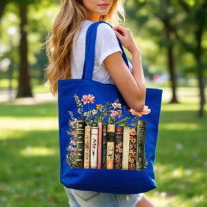 May include: A blue tote bag featuring a floral and book design. The tote bag has a vibrant illustration of colorful flowers and a row of vintage books. The bag is carried over the shoulder.