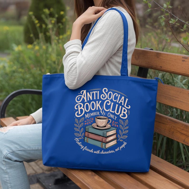 May include: A royal blue tote bag with a zipper closure. The bag features the text "Anti Social Book Club Member Only" with a graphic of books and a coffee cup. The phrase "Making friends with characters, not people" is also included.