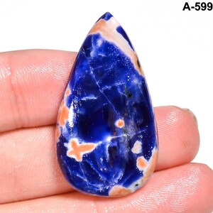 May include: A teardrop-shaped sodalite gemstone with a polished surface. The stone features a deep blue color with white and orange inclusions. The text "A-599" is visible in the upper right corner.
