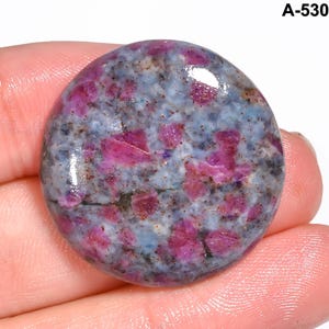 Pode incluir: Uma pedra preciosa redonda com uma superf&iacute;cie polida. A pedra apresenta uma mistura de cores, incluindo azul claro, cinza e rosa vibrante. As &aacute;reas rosa parecem ser inclus&otilde;es de rubi dentro da pedra. O texto "A-530" &eacute; vis&iacute;vel no canto superior direito.