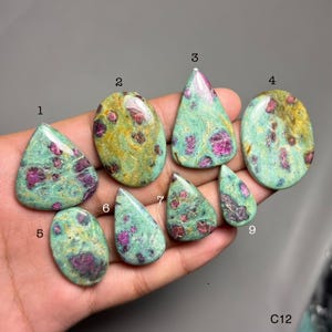 May include: Nine polished ruby zoisite gemstones in assorted shapes. The stones display green, yellow, and pink colours. Each gemstone has a unique pattern and texture, ideal for jewellery making.