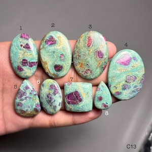 Puede incluir: Ocho piedras preciosas pulidas de varias formas, incluyendo ovaladas, en forma de lágrima y rectangulares. Las piedras presentan un color base verde-azulado moteado con inclusiones rojas vibrantes. La imagen está etiquetada como "C13".