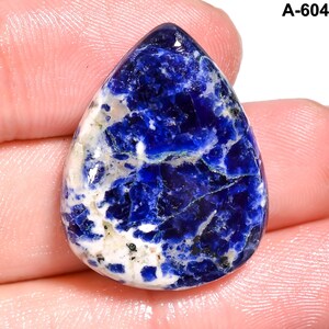 May include: A teardrop-shaped gemstone with a deep blue hue, marbled with white and gray patterns. The stone has a polished surface, reflecting light. The top right corner of the image has the text "A-604".