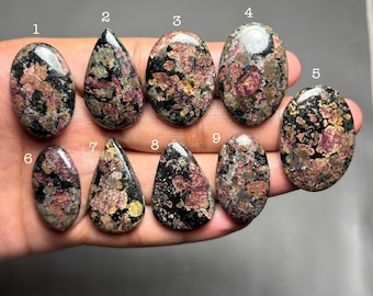 May include: Nine polished cabochon gemstones with a mottled pattern of black, dark green, and magenta-pink mineral inclusions. Each stone is numbered from one to nine, with varying oval and teardrop shapes, labeled with the code C134 at the bottom.