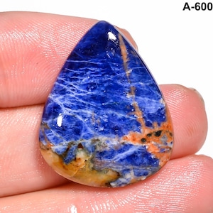 May include: A teardrop-shaped sodalite gemstone with a deep blue hue, veined with white and accented by orange and brown streaks. The stone is polished and held in a hand. The text "A-600" is visible in the upper right corner.