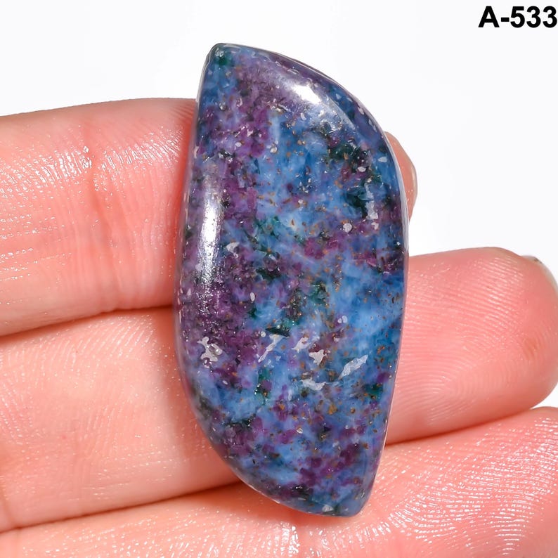 Pode incluir: Uma pedra preciosa polida com uma forma curva e alongada. A pedra apresenta uma mistura de cores, incluindo azul profundo, roxo e toques de verde. A superf&iacute;cie tem uma apar&ecirc;ncia manchada com um acabamento brilhante. O texto "A-533" &eacute; vis&iacute;vel.