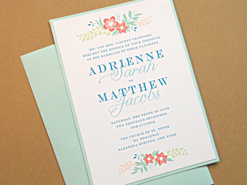 May include: A wedding invitation with a light blue border and floral accents. The invitation is for the wedding of Adrienne Sarah to Matthew Jacobs on Saturday, June 10th, 2017 at 1:00 PM at the Church of St. Peter in Saratoga Springs, New York.