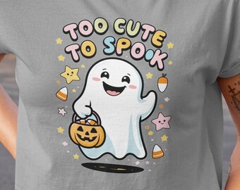 Puede incluir: Una camiseta corta gris con la frase "TOO CUTE TO SPOOK" en colores pastel. La camiseta presenta un fantasma de dibujos animados sosteniendo una calabaza de Halloween, rodeado de estrellas y caramelos. Un divertido diseño temático de Halloween.
