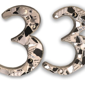 May include: A pair of black and white mosaic house numbers, each shaped like the number 3, creating the number 33. The mosaic is made of small pieces of glass and paper.