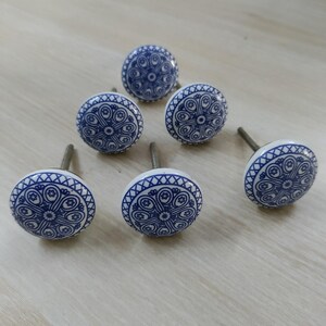 May include: Six white and blue ceramic cabinet knobs with a decorative floral pattern. The knobs have a round shape and are approximately 1.5 inches in diameter. The blue design is set against a white background, creating a contrasting visual appeal.
