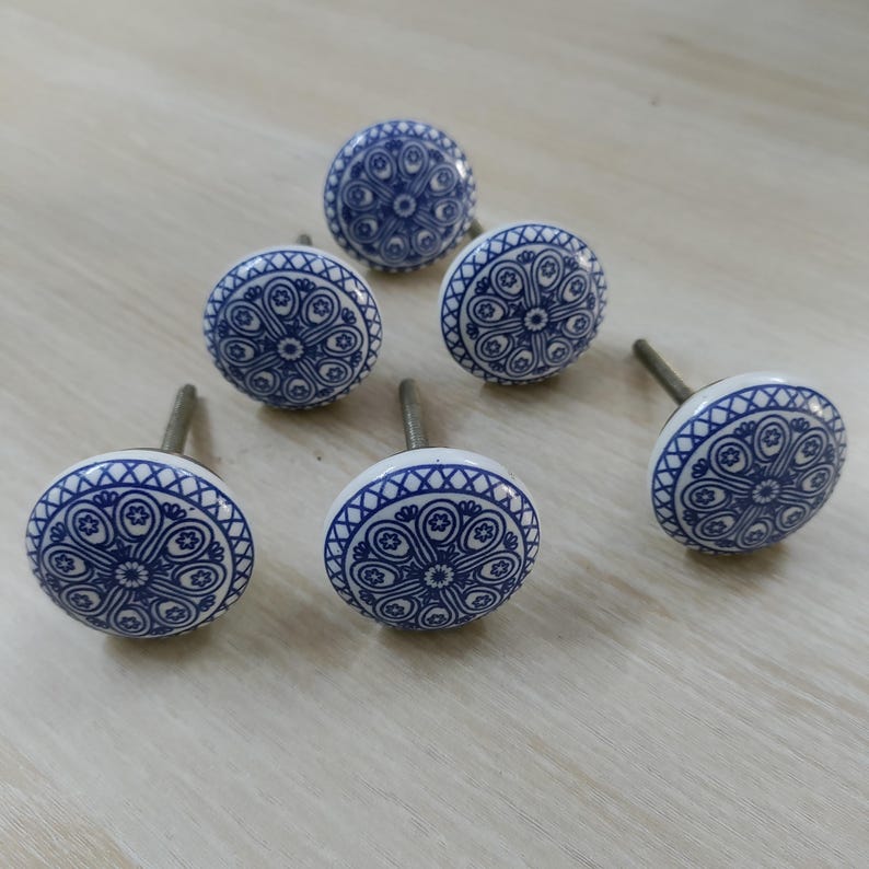 May include: Six white and blue ceramic cabinet knobs with a decorative floral pattern. The knobs have a round shape and are approximately 1.5 inches in diameter. The blue design is set against a white background, creating a contrasting visual appeal.