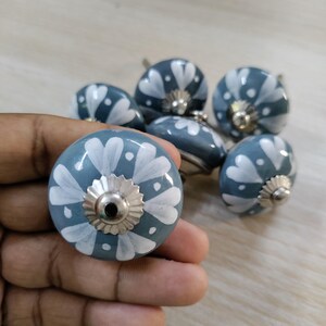 May include: A collection of six blue ceramic cabinet knobs with white floral designs. Each knob features a silver-colored metal base. The knobs are round and have a hand-painted appearance, suitable for furniture or decor.