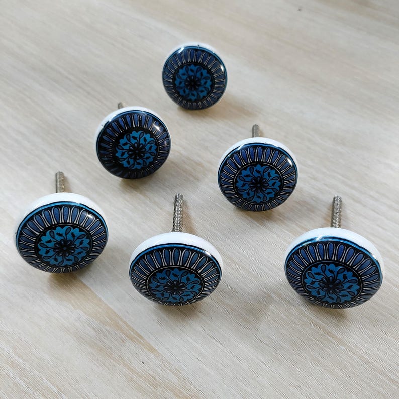 May include: Six decorative cabinet knobs with a white base and a blue floral design. The knobs have a silver screw for mounting. The floral design features shades of blue and black, creating a striking contrast.
