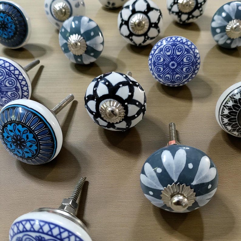May include: A collection of decorative ceramic cabinet knobs in various designs. The knobs feature patterns in blue, white, and black, with silver-toned metal hardware. The designs include floral, geometric, and abstract motifs, suitable for furniture or home decor.