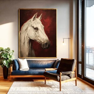 Pu&ograve; includere: Grande dipinto incorniciato di una testa di cavallo bianco su sfondo rosso scuro. L'opera d'arte &egrave; in una cornice dorata ed &egrave; appesa sopra un divano in pelle blu. La stanza ha un design moderno con una lampada da terra e una grande finestra.