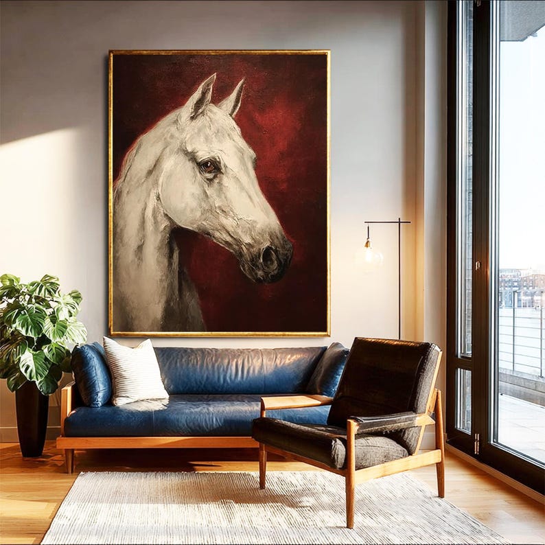Pu&ograve; includere: Grande dipinto incorniciato di una testa di cavallo bianco su sfondo rosso scuro. L'opera d'arte &egrave; in una cornice dorata ed &egrave; appesa sopra un divano in pelle blu. La stanza ha un design moderno con una lampada da terra e una grande finestra.
