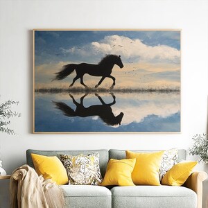 May include: A framed print shows a black horse galloping across water, with its reflection mirrored below. The background features a blue sky with white clouds and a sunset. The artwork is displayed above a grey sofa with yellow cushions.