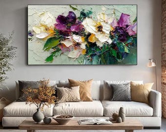May include: A framed floral painting with thick brushstrokes. The artwork features a bouquet of flowers in shades of white, yellow, and purple, set against a textured, light green background. Green leaves add contrast. The painting is displayed above a sofa.